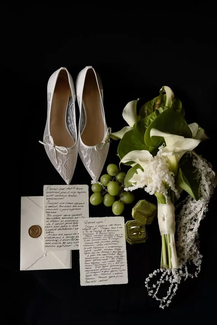 Satin heels, a calla lily bouquet and handwritten notes laid out on black