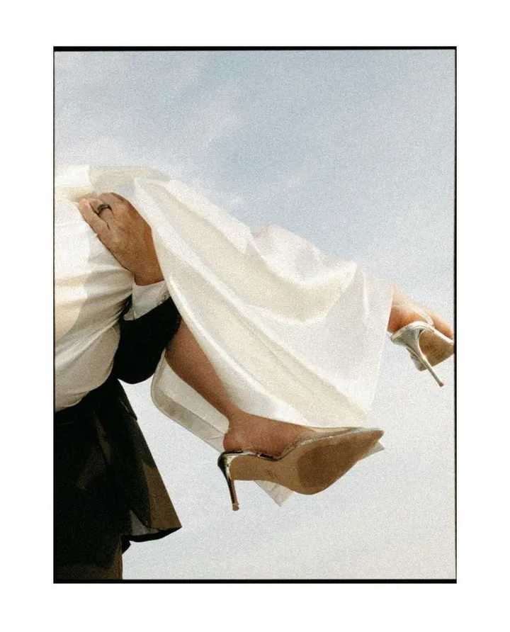 A bride lifted into the air against a pale sky, her veil and gown billowing